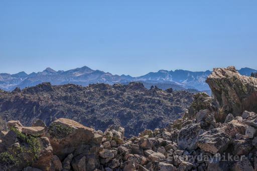 A layer of close by boulders followed by another large mound within the obsidian dome, with the jagged ridgeline of mountains seen in the distance.