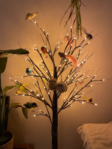 An artificial tree with no leaves and a bit of fake snow. It is decorated with lights and a couple of colorful birds. 